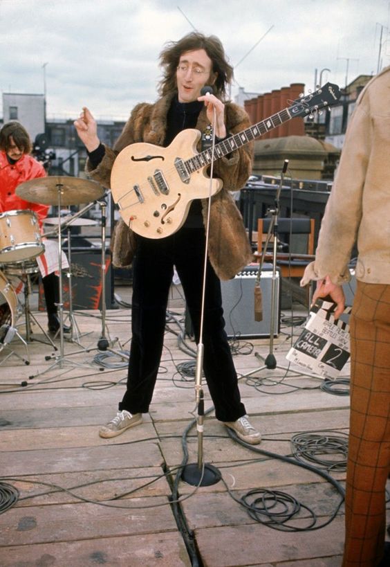 John Lennon stojący na dachu w Londynie. Ubrany w futrzany płaszcz, gra na gitarze Epiphone Casino.
